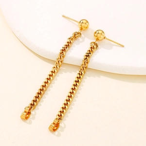 Detailed view of gold Cuban link chain tassel earrings on a minimalist stone surface