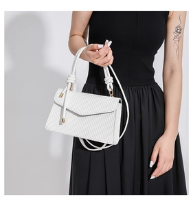 Detailed shot of white crossbody bag with textured surface and knotted handle detail