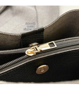 Detail view of smooth golden metal zipper and magnetic closure on black leather handbag