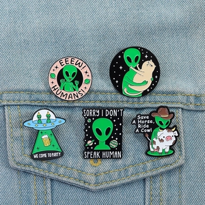 Detail of five alien enamel pins on denim jacket showing UFO and cow cat motifs