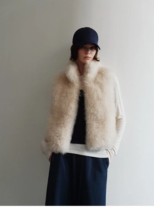 Detailed texture of plush beige faux fur vest worn by model against a neutral wall