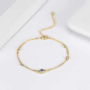 Detail shot of golden double-layer bracelet with blue evil eye pendant and adjustable chain