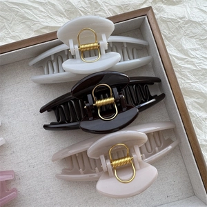 Minimalist curved hair claws in neutral colors displayed in a rustic wooden tray
