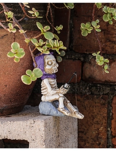 Detalle macro de figura de esqueleto con capa morada y caña de pescar sobre base de piedra