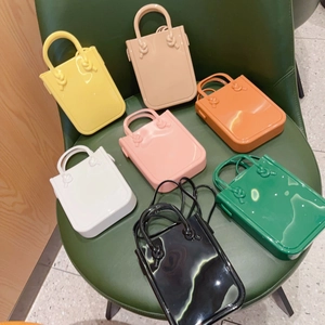 Top view of colorful PVC jelly handbags in seven vibrant shades on a green leather chair