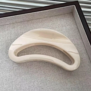Close-up of a large hollow curved cream hair claw clip on a textured linen display tray