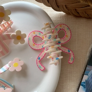 Detailed view of polka dot bow claw clip and floral hairpins in a ceramic dish
