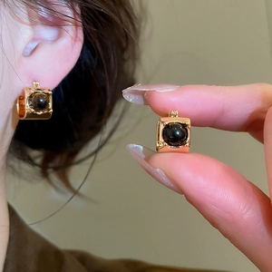 Close-up of gold-plated tiger eye earrings with round black gemstone in square frames