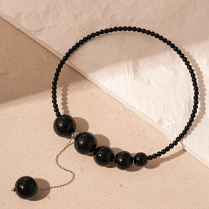 Détail du collier vintage en perles noires avec un pendentif élégant à pompon métallique