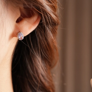 Detail of oval purple gemstone earring with zircon halo worn by a female model