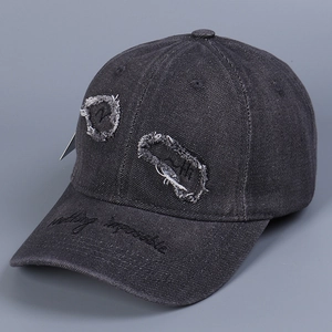 Dettaglio del cappellino da baseball in denim nero lavato con strappi e ricamo