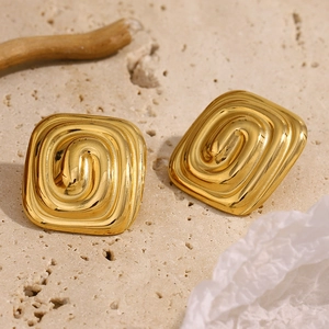 Gros plan de boucles d'oreilles carrées dorées à texture spirale sur pierre et bois