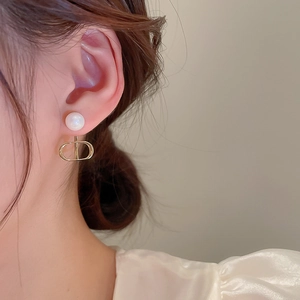 Close-up of pearl stud earrings with gold letter D pendant worn by a female model