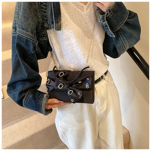 Detail of black satin clutch featuring a rhinestone bow and golden chain strap for evening