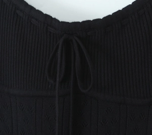 Détail de robe noire en tricot avec col à nouer et motifs en maille ajourée