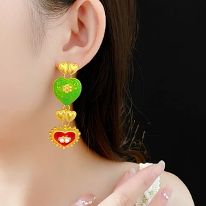 Detail of vintage heart earrings with green and red enamel and pearl accents on model