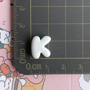 Macro shot of white resin letter K mini accessory on a grid cutting mat showing size