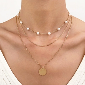Detail of layered gold necklace featuring pearl beads and round metallic pendant on model