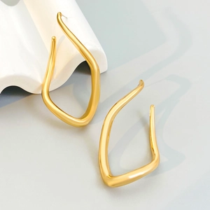 Golden irregular geometric twisted hoop earrings displayed on white artistic wave stand