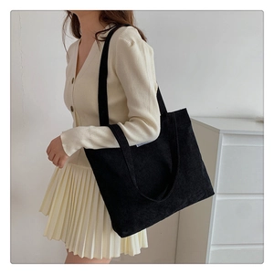 Side view of a black corduroy tote bag worn by a model in a minimalist setting