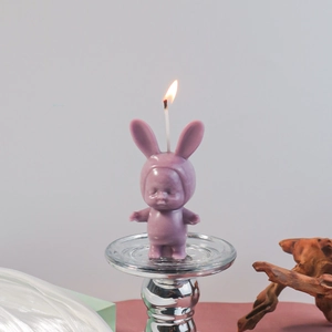 Detail of a purple bunny-ear baby candle lit on a silver glass tray with a cozy background