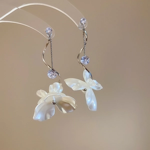 Détail de boucles d'oreilles argentées avec zircon et élégants pompons floraux blancs