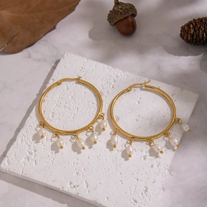 Elegant gold hoop earrings with natural freshwater pearl charms on marble background
