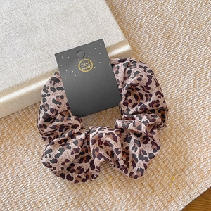 Leopard print scrunchie on woven mat next to a book, vintage aesthetic hair accessory