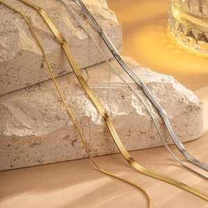 Polished gold and silver snake bone chain necklaces displayed on natural stone