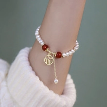 Detail of freshwater pearl bracelet featuring a gold Fu pendant on a woman's wrist