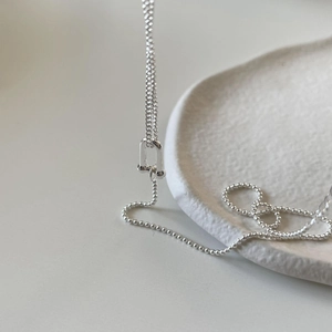 Macro shot of silver ball chain necklace with U-shaped buckle on a white ceramic plate