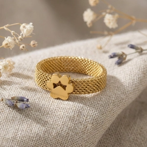 Macro view of gold mesh woven ring featuring a dangling cutout pet paw charm on linen
