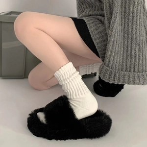 Close-up of black fuzzy faux fur slippers paired with white ribbed cotton mid-calf socks