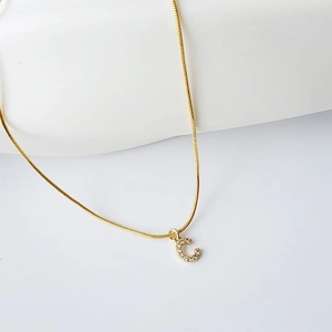 Close-up of golden letter C pendant with sparkling zircons on a snake chain necklace