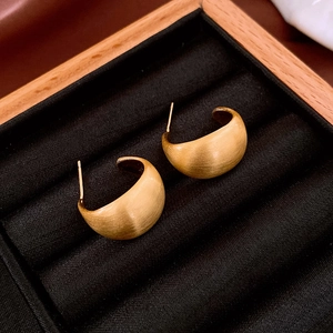Detail of 14K gold plated earrings with a wide C-shape and brushed matte texture