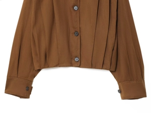 Detail of dark brown jacket featuring button closure and pleat accents on the hem