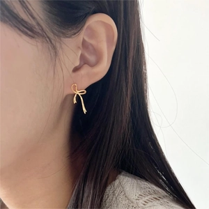 Macro close-up of a delicate gold bow earring worn on the earlobe with minimalist style