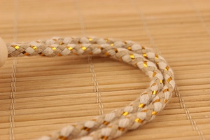 Macro shot of 8ml perfume bottle hanging rope woven with beige cotton and gold metallic silk