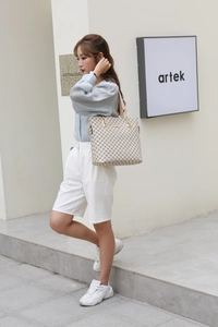 Detail of beige tote bag with geometric pattern and metallic hardware in outdoor setting