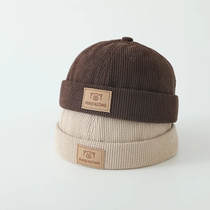 Close-up of baby knit hats featuring textured stripes and premium leather bear patches