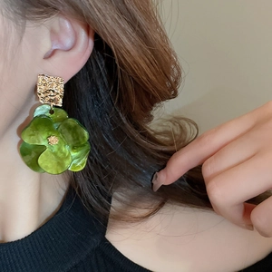 Macro detail of green acrylic flower earrings with textured gold geometric metal studs
