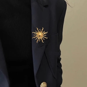 Elegant gold sunburst brooch with radiant light rays pinned on a dark formal suit blazer