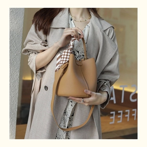Brown leather bucket bag with plaid silk scarf and shoulder strap held by a model