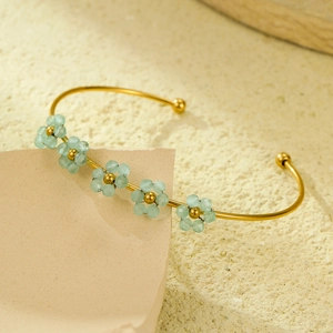 Dettaglio del bracciale rigido dorato in acciaio inossidabile con fiori di perline blu