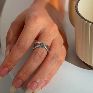 Macro detail of silver geometric double ring with hollow leaf chain design on hand