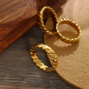 Three stacked 18K gold plated twisted rope rings on a rustic wooden aesthetic surface