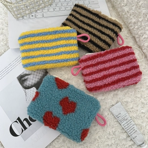 Flat lay of colorful plush heart-patterned makeup bags on soft white carpet texture