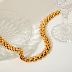 Detailed view of an 18K gold-plated stainless steel woven chain necklace on glass