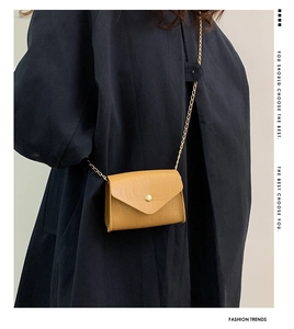 Detail of yellow crocodile pattern leather bag with gold chain strap on dark coat