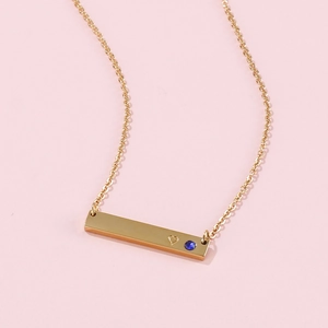 Close-up of gold bar pendant with heart cutout and blue birthstone on a fine chain